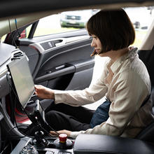 A woman sits in the passenger side of a parked car, looking at a large monitor attached to the dashboard. 