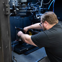 View from over a man's shoulder shows him adjusting scientific equipment inside a cabinet. 