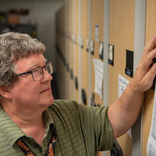 Doug White stands looking at a printed-out list taped to the end of a library shelf. 