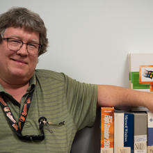 Doug White poses with his arm resting on a row of software boxes. 