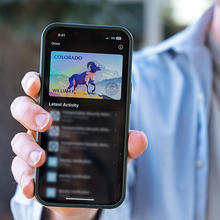 Close-up of a smartphone held in a person's hand, showing a Colorado mobile driver's license with an image of a bighorn sheep. 