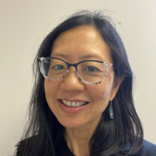 A woman with long black hair and glasses, smiling for a photo. 