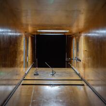 View from inside a square tunnel looking out into a dark space. Near the end of the tunnel, two small devices are attached to the floor. 