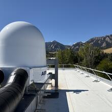 A white dome is installed on the roof of a building with mountains in the background. 