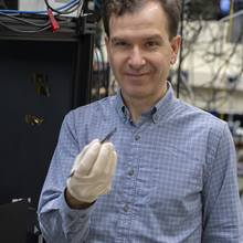 A researcher stands in the lab, holding a chip with tweezers in his gloved hand. 