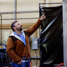 Two men in safety glasses stand in the lab looking at a large metal cylinder.
