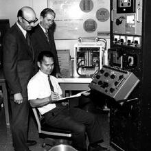 Three men sit at a dashboard