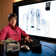 Woman with her hand on a fingerprint scanner with a screen in the background showing her fingerprint scans