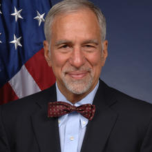 Headshot of Phillip Singerman in a bowtie. American flag in background