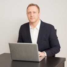 Jack Glover sitting at a laptop and smiling at the camera. 