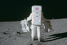 Buzz Aldrin (from the back) in his moonsuit carrying the NIST laser retroreflector to install it on the moon