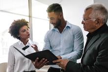 Two men and a woman standing discussing documentation they are holding.