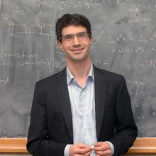headshot of Jake Taylor in front of a chalkboard with mathematical equations behind him.