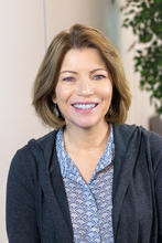 A headshot of Ellen Ryan, a woman, smiling, wearing a blue shirt with short brown hair