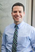 This is a headshot of Jeremy Glenn, a man wearing a blue shirt and green tie