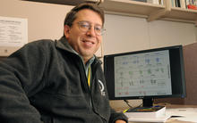 John Butler in his lab in front of a computer monitor with graphics on it