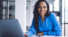 Woman sitting at a table while leaning on her hand and using her laptop to apply to become a Baldrige examiner.