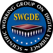 A black ring with the words in white reading around the circle from bottom clockwise :  Scientific Working Group on Digital Evidence ~ and inside the ring a blue background with the letters SWGDE over a brownish red rhombus like a square table if you are facing a corner and white prongs coming down that look like upside down bottles and perhaps represents a computer chip, then along the bottom 7 white stars    