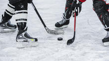Photo of two players with hockey sticks and a puck on ice