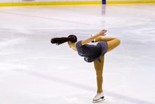 Photo of a female figure skater doing a twirl holding her foot in the air with her right hand