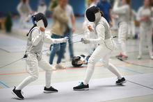 2 people in white fencing outfits and helmets are fencing in a competition