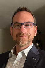 smiling man in black suit wearing glasses