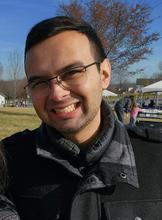smiling man outside in a black coat wearing glasses