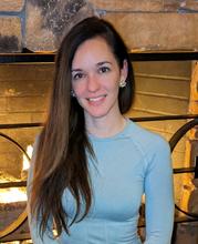 Kristina Rigopoulos poses sitting in front of a fireplace.