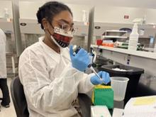 Diane Nelson, a person in a mask and lab coat, works with plastic test tubes at a lab bench.