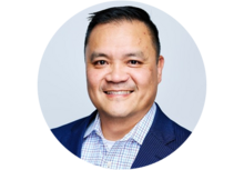 Headshot of Norman Wong, a man with short black hair, smiling, wearing a collared button up shirt and a blue suit jacket.