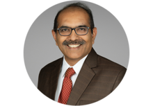Professional Headshot of Swamy Sriperumbudur, a man with short dark hair and a mustache, smiling, wearing a suit and red tie.