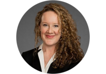 Professional headshot of Emma Marion, a woman with long curly blonde hair, wearing a black blazer with a white collar, smiling.