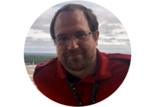 Headshot of Andrew Perkinson, a man with short brown hair, wearing glasses, a red polo, and a lanyard, smiling, standing outside.