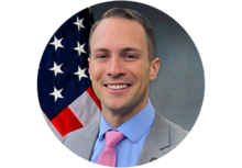Professional headshot of SETH R. WHITWORTH, a man wearing a suit and tie, smiling in front of an American flag.