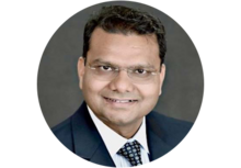 Professional headshot of Jai S. Arun, a man with short dark hair and glasses, smiling, wearing a suit and tie.
