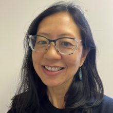 A woman with long black hair and glasses, smiling for a photo. 