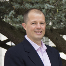 David Holbrook, a man with short hair, wearing a blazer and collared shirt, standing outside, smiling.