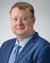 William Brad O'Dell smiling for a professional headshot against a light gray studio backdrop.