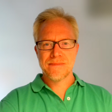 Benjamin Long, a man with light blonde hair, a beard, and glasses, posing for a headshot. 