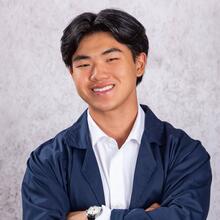Professional headshot of Ryan Giang, a young man with short black hair, smiling, wearing a white collared shirt, navy blue jacket and watch.