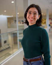 Professional portrait of Theresa Thomas, a young woman with short dark hair and glasses, wearing a green turtleneck, smiling.
