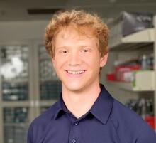 Headshot of Rion Wendland, a young man with red hair, smiling, and wearing a collared blue shirt.