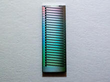 Tiny rectangular chip holds lines of even tinier rings and reflects a rainbow of colors. 