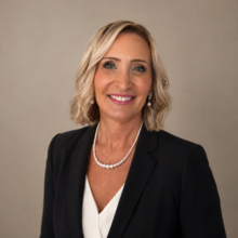 Professional portrait of Frannie Johnson, a woman with short wavy blonde hair, smiling, wearing a black blazer and white blouse.
