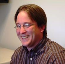 Justin Gorham, a person with short brown hair and glasses, smiling for the camera. 