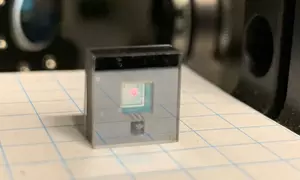A tiny chip encased in clear plastic sits on a piece of graph paper. 