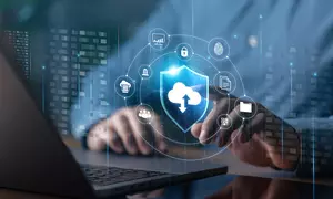 Illustration shows cloud, cybersecurity and identity icons floating over an open laptop with a person's hands at the keyboard.