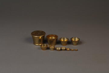 11 gold weights on a gray background