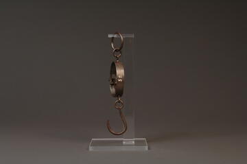 Side view of steel mancur balance hanging from clear plastic stand