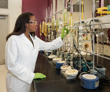 A chemist stands in a white coat before a bunch of beakers.